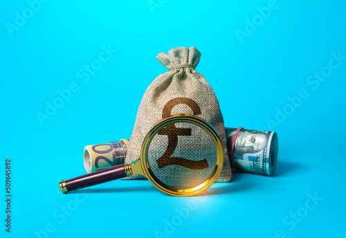 British pound sterling money bag and magnifying glass. Anti money laundering, tax evasion. Deposit or loan terms conditions. Find investment funds for business project. Investigating capital origins. photo