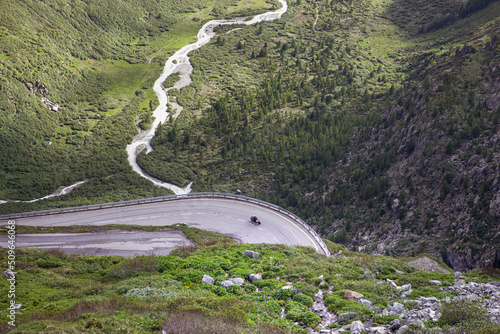 Mountain road. View on serpentine road on mountain pass and beautiful alps landscape. Motorcycle driver on a bend from above with green summer valley of the river. Furka Pass route in swiss alps.