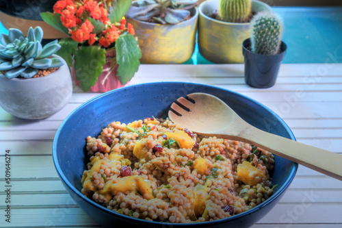 Side view of mango couscous salad on white natural wood table