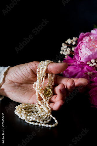 hand holding a necklace. Bouquet of white and pink peony on a black background.