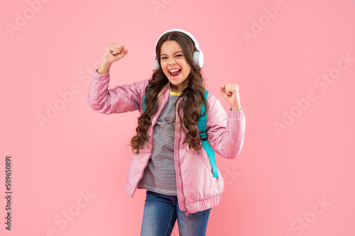 successful child listen music in headphones and carry backpack on pink background, music