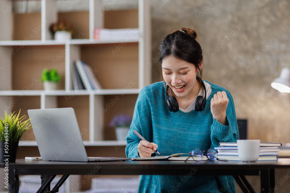 Young attractive female student writer scribing notes to a textbook to prepare for the Exam preparation, Asian girl sitting homework on a laptop computer, making a plan for tomorrow creating a list Young attractive female student writer scribing notes to a textbook to prepare for the Exam preparation, Asian girl sitting homework on a laptop computer, making a plan for tomorrow creating a list