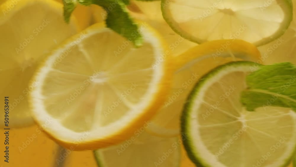 Lemon and lime cocktail, cooking cold lemonade, citrus fruits in water on yellow background, shooting of carbonated water with floating sliced fruits. Lemon and lime cocktail, cooking cold lemonade, citrus fruits in water on yellow background, shooting of carbonated water with floating sliced fruits.