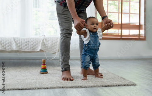 фотографія Cute smiling African baby girl learning to walk with father support and holding her hands