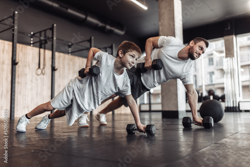 Healthy family concept. Father trainer and teenager son training with dumbbells in gym. Fitness, sports, active lifestyle