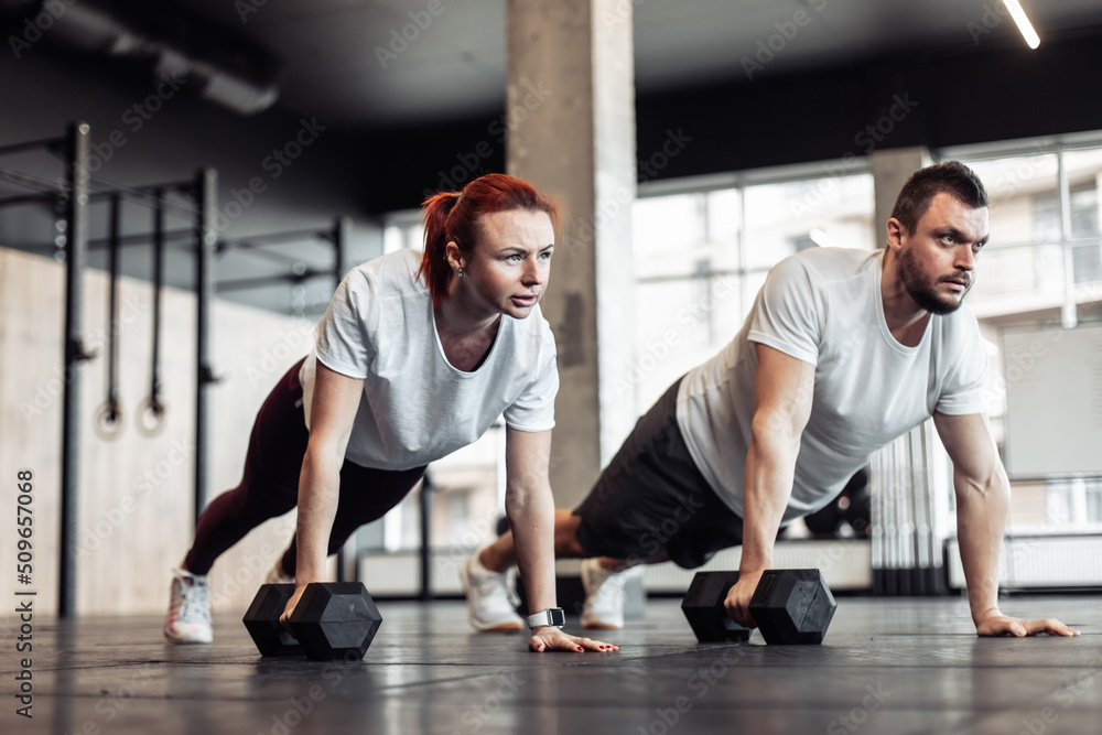 Athletic man and woman doing intensive workout together with dumbbells in a modern gym. Functional training. Bodybuilding and fitness. Healthy lifestyle