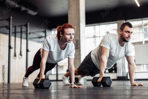 Athletic man and woman doing intensive workout together with dumbbells in a modern gym. Functional training. Bodybuilding and fitness. Healthy lifestyle © splitov27