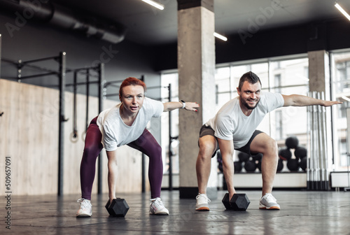 Athletic man and woman doing intensive workout together with dumbbells in a modern gym. Functional training. Bodybuilding and fitness. Healthy lifestyle