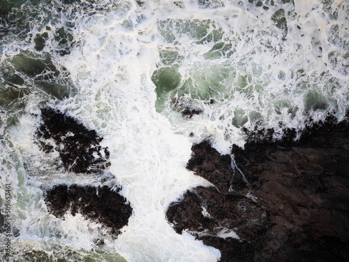 View from above. Bubbling white ocean waves crash against the rocky shore. The beauty and majesty of nature. Abstraction. There are no people in the photo. Ecology, environmental protection. © Anton