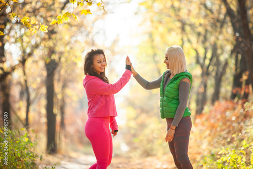 Two fitness women give five to each other in autumn forest. Healthy lifestyle