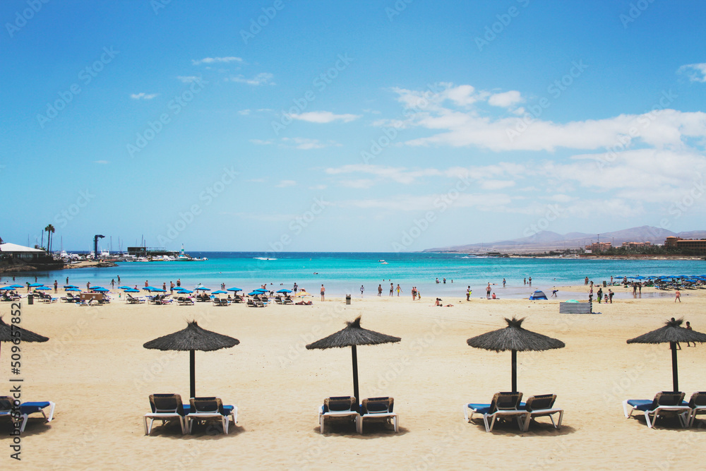 In the open air, umbrellas and sun loungers lined up on the sand on the beach, open sea and sky.