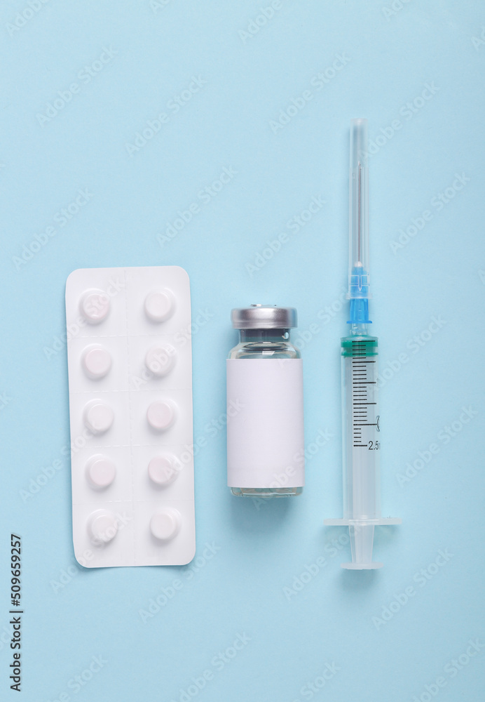 Vaccination, treatment concept. Vaccine bottle with blank label, syringe and white blister of pills on blue background. Top view, flat lay Vaccination, treatment concept. Vaccine bottle with blank label, syringe and white blister of pills on blue background. Top view, flat lay