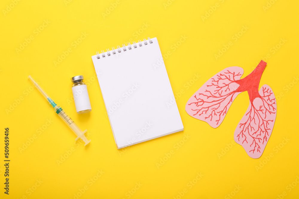 Vaccine bottle with syringe, notebook and anatomical lungs on yellow background. Top view Vaccine bottle with syringe, notebook and anatomical lungs on yellow background. Top view
