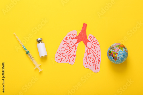 Vaccine bottle with syringe and anatomical lungs, globe on a yellow background. Pandemic covid 19