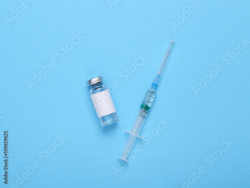 Vaccine bottle with a blank label for the brand and syringe on blue background.
