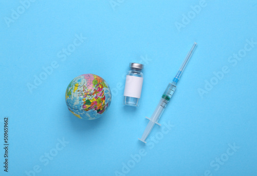 Vaccine bottle with a blank label for the brand and syringe, globe on blue background. Pandemic covid 19, vaccination