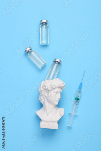 David bust and Vaccine bottle with syringe on blue background. Covid 19 vaccination