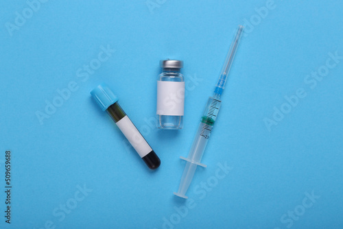 Testing and vaccination, covid 19 treatment. Vaccine bottle and blood test with blank label for brand and syringe on blue background. Top view. Flat lay