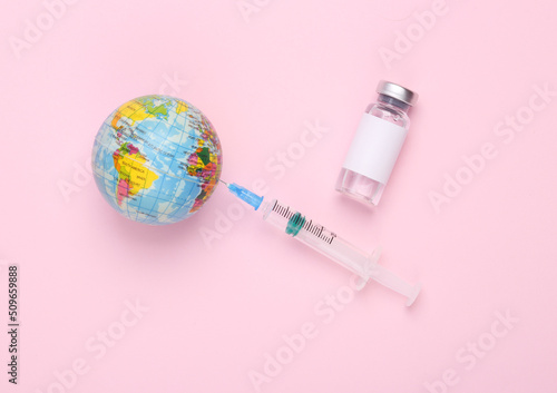 Vaccine bottle with a blank label for the brand and syringe, globe on pink background. Pandemic covid 19, vaccination