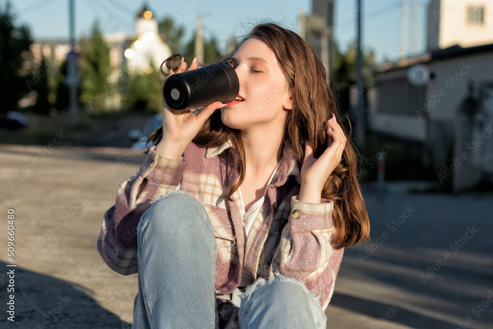 A beautiful woman with a cup in her hand on the street in the city. Portrait. Youth culture