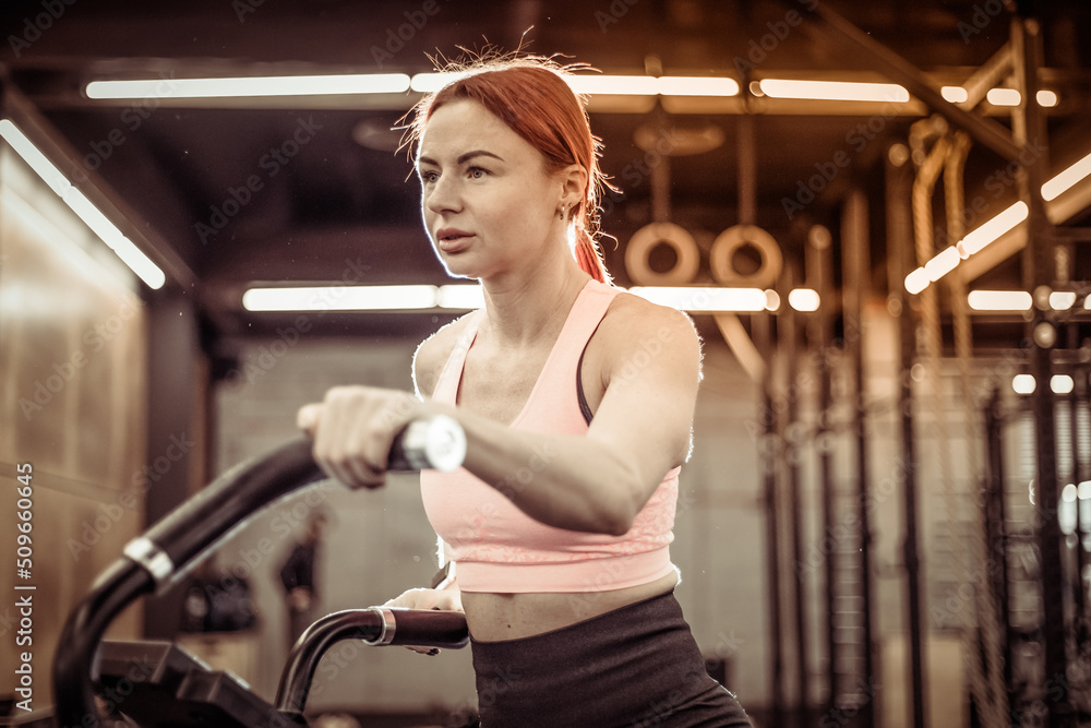Redhead fit woman doing intense cardio training on exercise bike Redhead fit woman doing intense cardio training on exercise bike