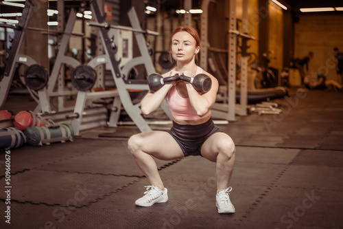 Intensive workout red-haired woman with kettlebells in her hand in modern gym