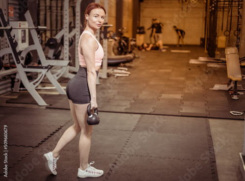 Intensive workout red-haired woman with kettlebells in her hand in modern gym