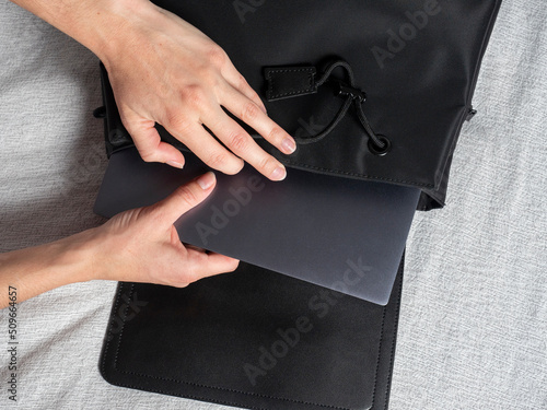 Close-up of a woman's hand putting a gray laptop in a black bag, the concept of working from home, freelance, remote work. Selective focus. top view, flat lay