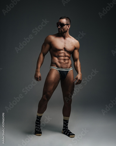 Naked sportsman in sunglasses standing in studio