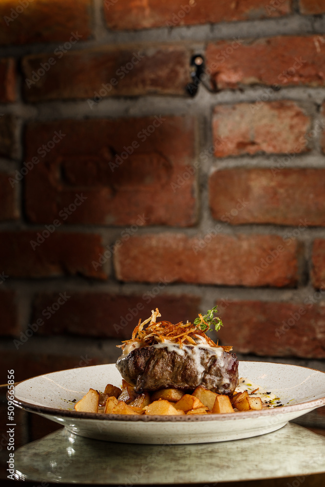 Grilled steak with baked golden potatoes served with crispy onion on top on a brick background. Delicious Recipe.