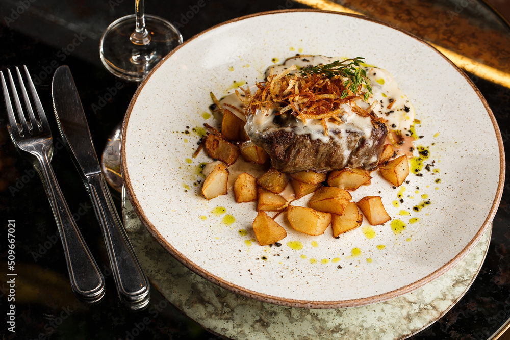 Grilled steak with baked golden potatoes served with crispy onion on top on a brick background. Delicious Recipe.