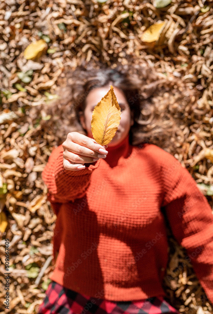 Young happy woman gathering leaves in autumn forest