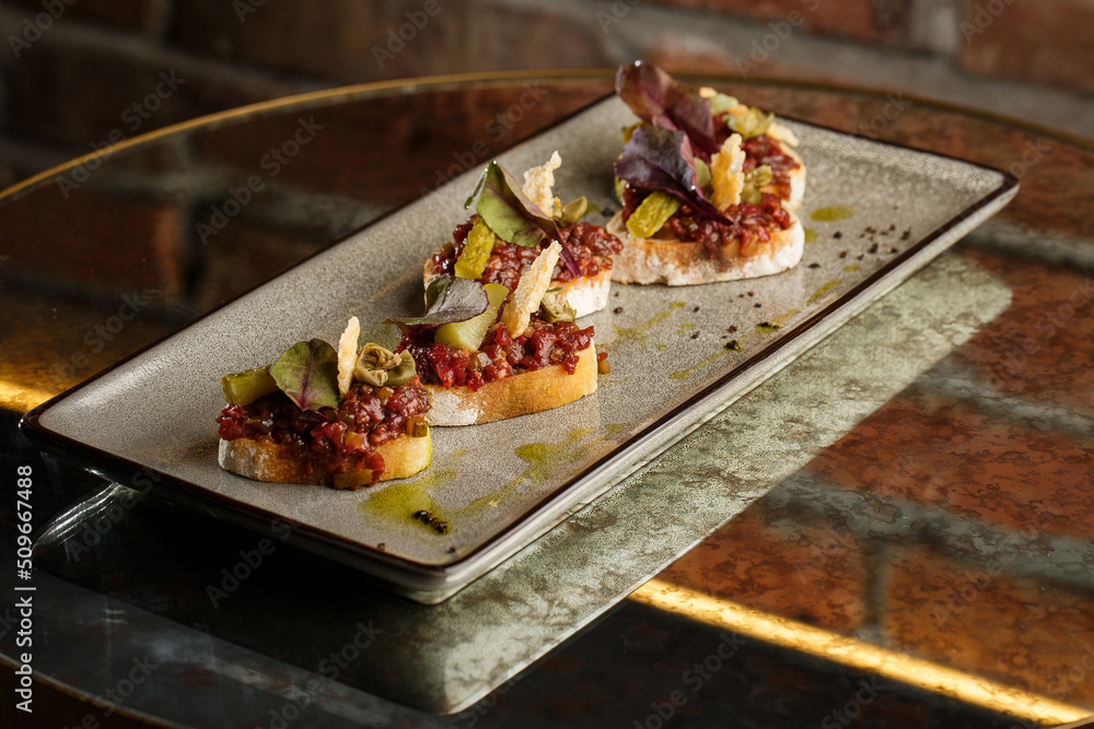 Four bruschettas with beef tartare on a plate, Crostini with Beef Tartare, beef Bruschetta, sandwich with raw gourmet beef.