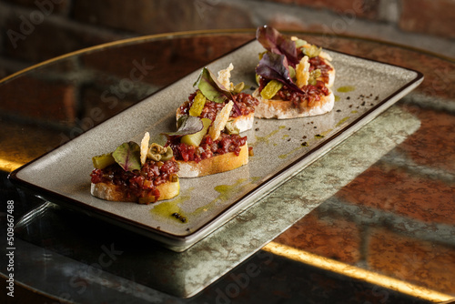 Obraz na płótnie Four bruschettas with beef tartare on a plate, Crostini with Beef Tartare, beef Bruschetta, sandwich with raw gourmet beef. w salonie