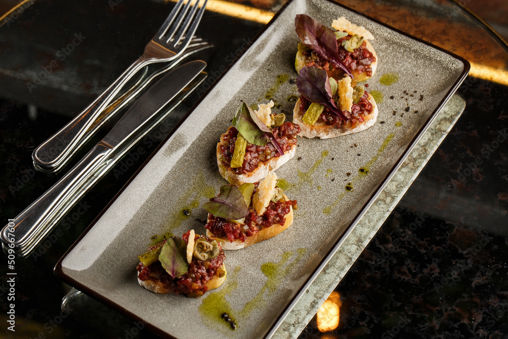 Four bruschettas with beef tartare on a plate, Crostini with Beef Tartare, beef Bruschetta, sandwich with raw gourmet beef.