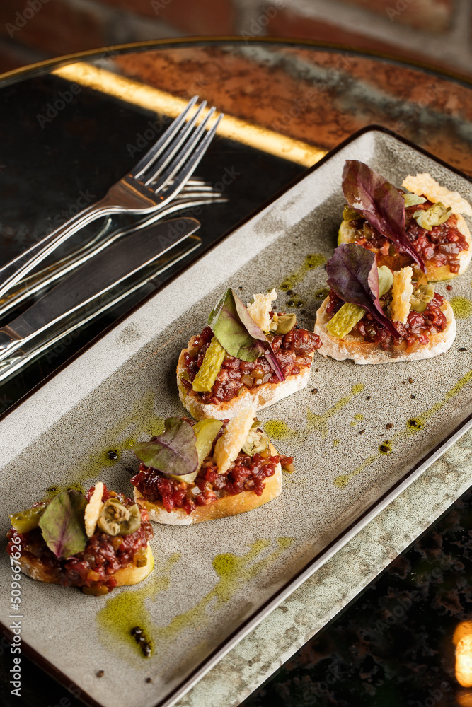 Four bruschettas with beef tartare on a plate, Crostini with Beef Tartare, beef Bruschetta, sandwich with raw gourmet beef.