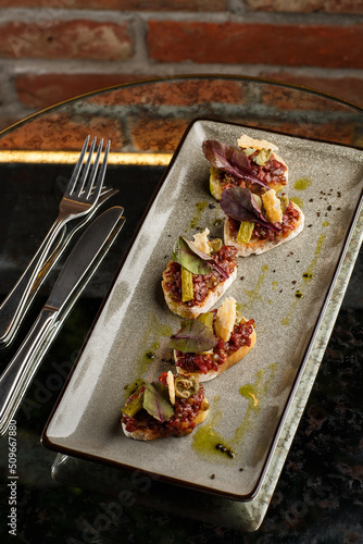 Four bruschettas with beef tartare on a plate, Crostini with Beef Tartare, beef Bruschetta, sandwich with raw gourmet beef.