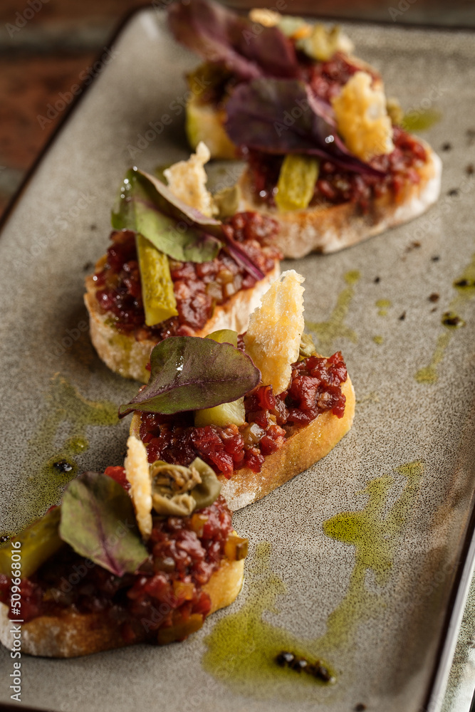 Four bruschettas with beef tartare on a plate, Crostini with Beef Tartare, beef Bruschetta, sandwich with raw gourmet beef.