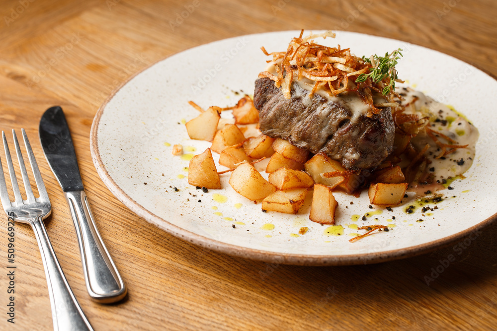 Grilled steak with baked golden potatoes served with crispy onion on top on a brick background. Delicious Recipe.