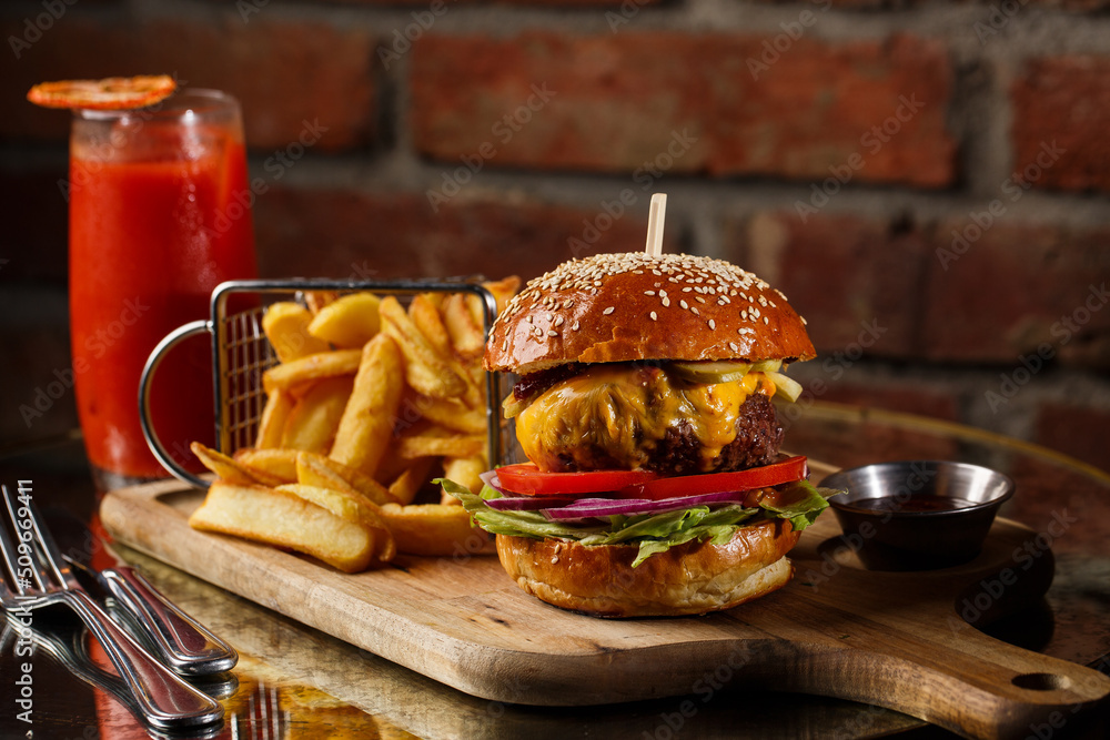 Big cheeseburger with french fries isolated on white background. Hamburger with beef patty onion, tomato, lettuce pickles, melted cheddar, mustards, tomato jam, mayo