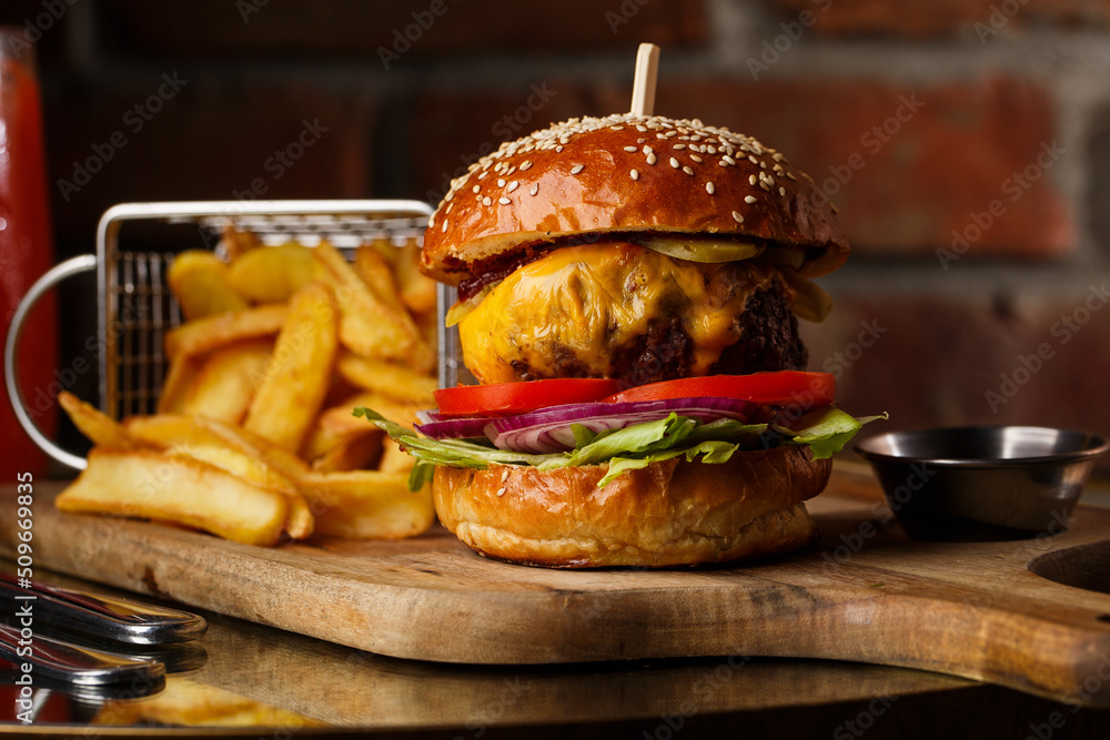Big cheeseburger with french fries isolated on white background. Hamburger with beef patty onion, tomato, lettuce pickles, melted cheddar, mustards, tomato jam, mayo