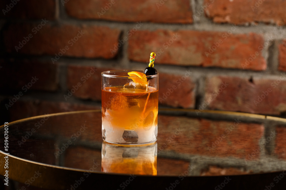 Crystal glass with bright cold alcoholic cocktail decorated with orange zest. Blurred background. Negroni cocktail.