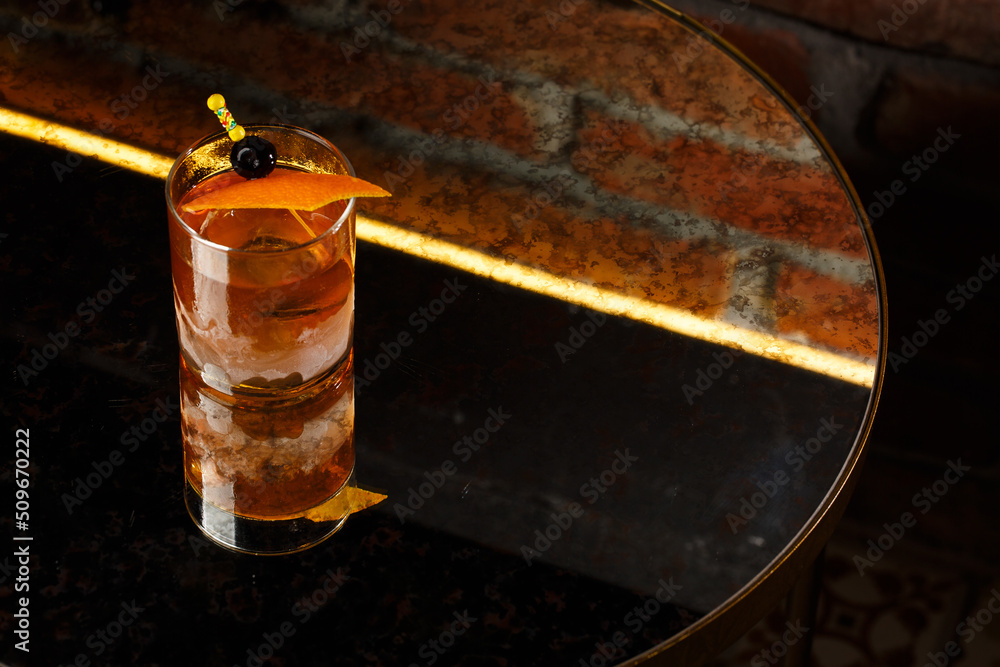 Crystal glass with bright cold alcoholic cocktail decorated with orange zest. Blurred background. Negroni cocktail.
