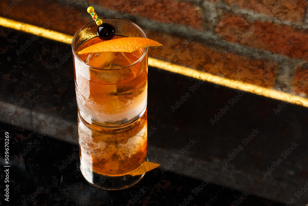 Crystal glass with bright cold alcoholic cocktail decorated with orange zest. Blurred background. Negroni cocktail.