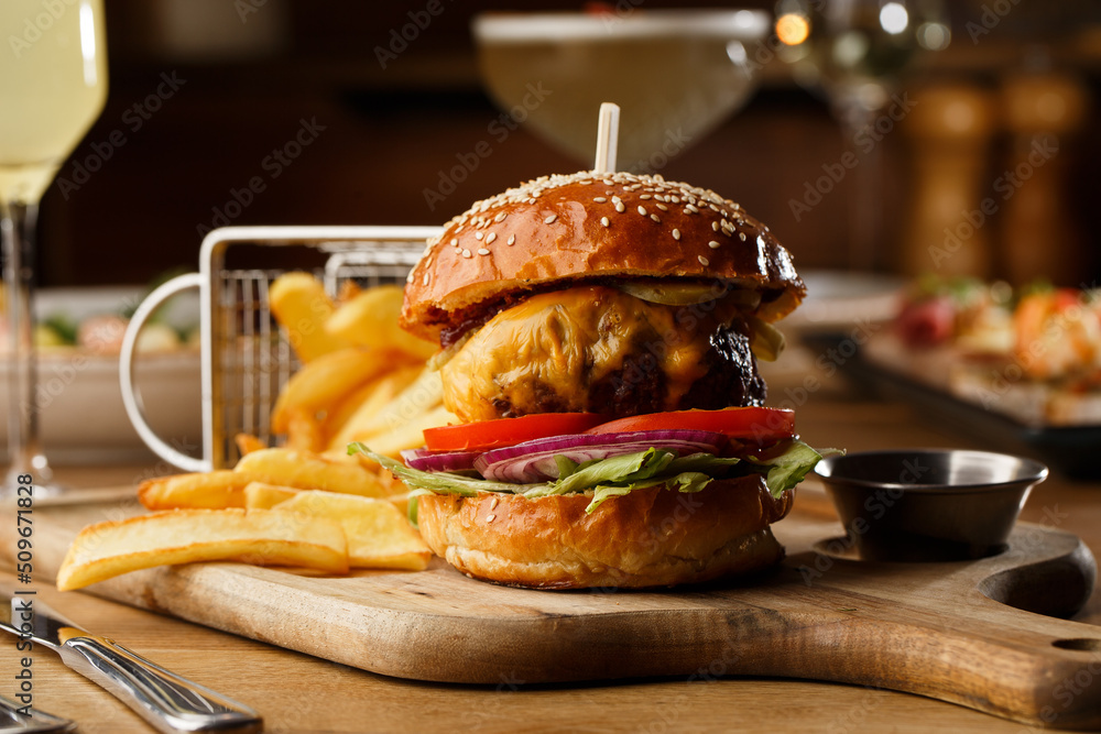 Big cheeseburger with french fries isolated on white background. Hamburger with beef patty onion, tomato, lettuce pickles, melted cheddar, mustards, tomato jam, mayo