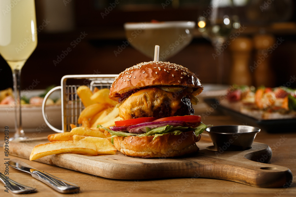 Big cheeseburger with french fries isolated on white background. Hamburger with beef patty onion, tomato, lettuce pickles, melted cheddar, mustards, tomato jam, mayo