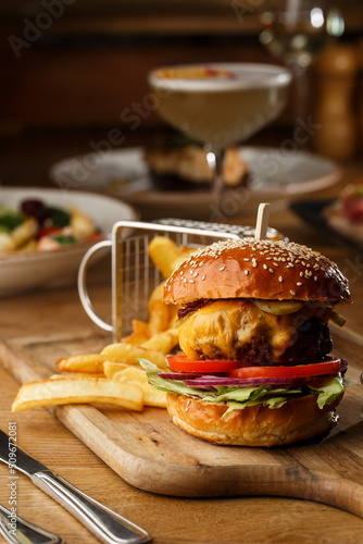 Obraz na płótnie Big cheeseburger with french fries isolated on white background. Hamburger with beef patty onion, tomato, lettuce pickles, melted cheddar, mustards, tomato jam, mayo w salonie