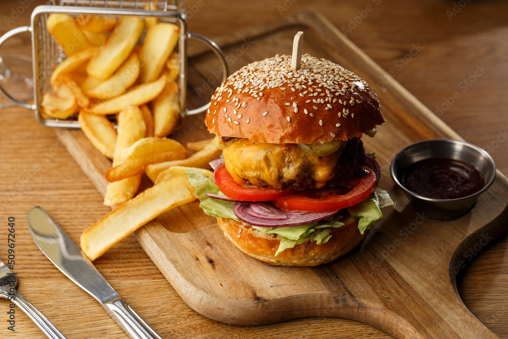 Big cheeseburger with french fries isolated on white background. Hamburger with beef patty onion, tomato, lettuce pickles, melted cheddar, mustards, tomato jam, mayo