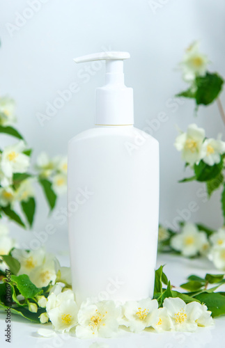 Bottle of cosmetic product on a background of jasmine. Selective focus.
