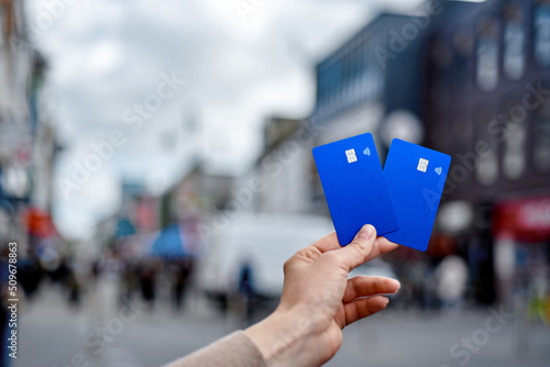 A young girl's hand holds two blue bank cards against the backdrop of a blurry street.
